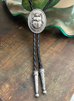 This awesome bolo tie has a meal beetle pendant. Quality guaranteed, picture does not do this buckle justice! The pendant piece measures 1 1/8'' x 1 1/4'' It can adjust lengths, 39'' in total length. The cord is genuine black woven leather.   We have matching belt buckles to pair! Men’s Leather Jewelry, Brown Bolo Ties As A Gift, Brown Bolo Tie For Gift, Silver Bolo Ties As A Gift, Bolo Tie Outfit, Beetle Pendant, Cowboy Jewelry, Cowboy Accessories, Cool Belt Buckles