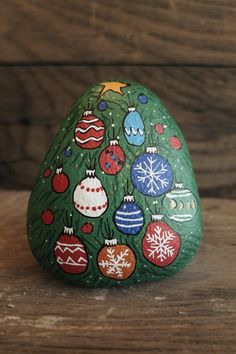 a painted rock with christmas ornaments on it sitting on a wooden table next to a wall