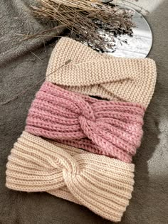 three knitted headbands are laying on the ground next to some dry grass