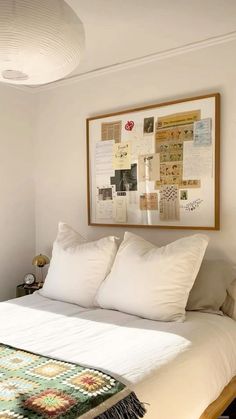 a bed with white linens and pillows in a small room next to a painting on the wall