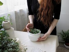 a woman with long red hair is holding a white bowl full of green plants in her hands