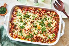 a casserole dish with meat, cheese and vegetables on it next to two wooden spoons