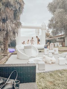 children playing in an outdoor play area with white furniture and palm trees on the lawn