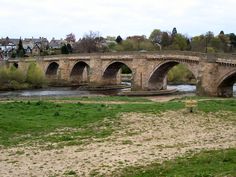 an old stone bridge over a river in the middle of a town with green grass