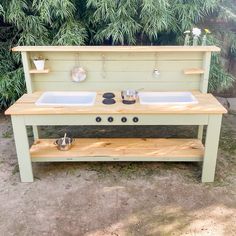 an outdoor kitchen with two sinks and pot holders on the outside wall, in front of some trees