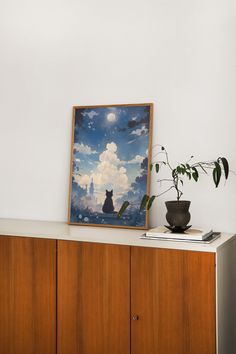 a painting sitting on top of a wooden cabinet next to a potted plant