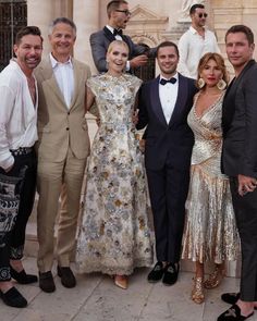 a group of people standing next to each other in front of a building wearing tuxedos