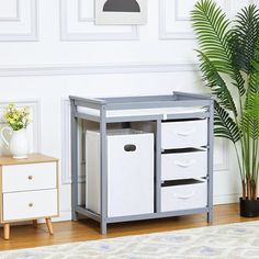 a baby changing table with drawers and storage bins on the bottom, next to a potted plant