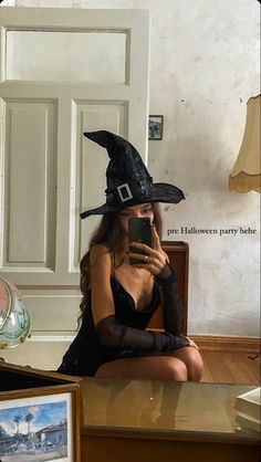 a woman sitting on the floor wearing a witches hat and holding a cell phone in her hand