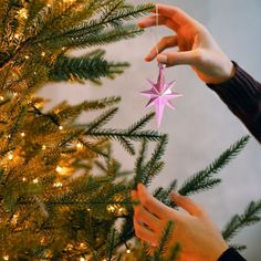 two hands reaching for a star ornament on a christmas tree