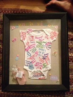 a baby's bodysuit is displayed in a shadow box with its name written on it