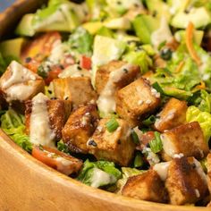 a salad with tofu and lettuce in a wooden bowl on a table