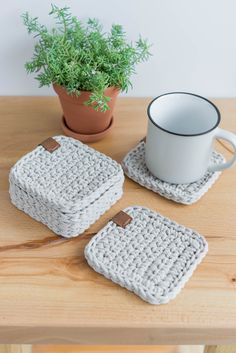 two crocheted coasters on a wooden table with a coffee cup and plant