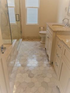 a bathroom with white cabinets and hexagonal tile flooring on the walls, along with a walk in shower