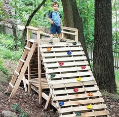 a young boy standing on top of a wooden slide in the woods with balls all over it