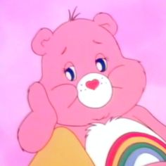 a pink teddy bear sitting on top of a rainbow colored pillow in front of a pink background