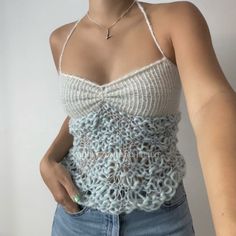 a woman wearing a crochet tank top with her hands in her pockets and one hand on her hip