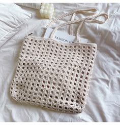 a crocheted white bag sitting on top of a bed next to a book