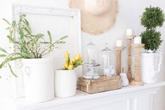 a white mantle topped with vases filled with flowers next to a hat and candle holder