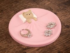 a teddy bear sitting on top of a pink plate next to two rings and a ring holder