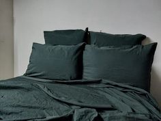 an unmade bed with green sheets and pillows