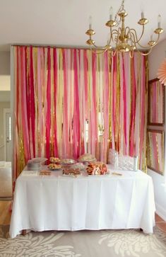 a table topped with cake and desserts under a chandelier next to a pink curtain