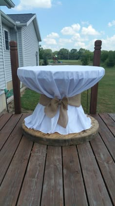 a table covered with a white cloth and brown bow sitting on top of a wooden deck