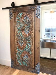 an intricately carved wooden door in a kitchen with wood floors and white walls, next to a stainless steel sink