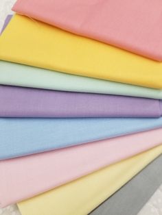 many different colors of fabric on a white tablecloth with the same color as the background