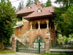 an old brick house with arched windows and iron fence around the front gate, surrounded by trees