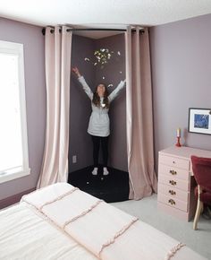 a woman standing in front of a window with her arms up and flowers flying from the ceiling