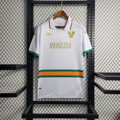 a white shirt hanging on a rack in front of a metal fence with an orange and green stripe