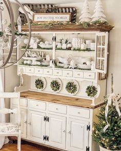 a white hutch with christmas decorations on top and wreaths hanging from the shelves