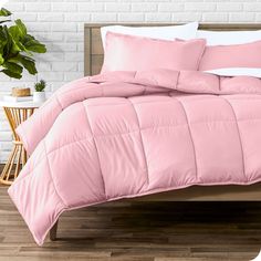 a bed with pink comforter and pillows on it next to a potted plant