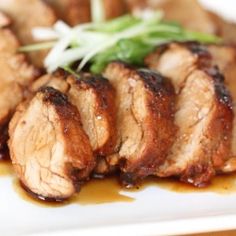 some meat is sitting on a white plate with sauce and green garnishes