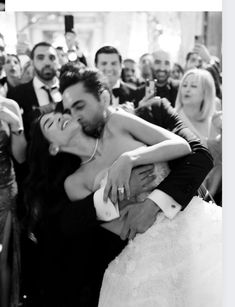 a bride and groom hugging each other in front of a group of people at a wedding