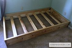 a wooden bed frame sitting on top of carpeted floor next to a blue wall