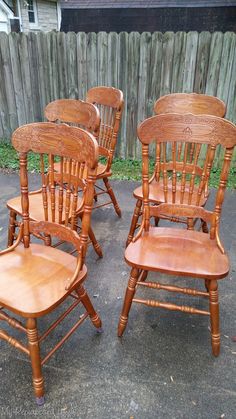 four wooden chairs sitting next to each other in front of a fenced backyard area