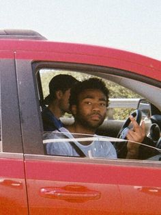 two men sitting in the drivers seat of a red car