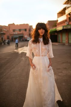 a woman standing in the middle of an empty street wearing a white dress and heels