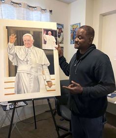 a man standing in front of a painting holding his hand up to the camera and pointing at it