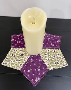 a white candle sitting on top of a table next to a purple and green placemat