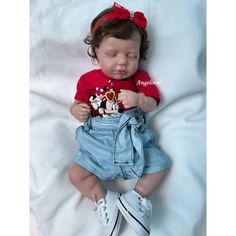 a baby doll that is laying down on a white sheet with a red shirt and mickey mouse t - shirt