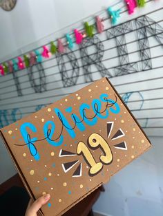 a person holding up a cardboard box with the word felices on it and decorations