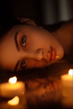 a woman laying on the ground with candles around her and looking up at the camera