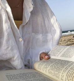 a woman reading a book on the beach with her hand resting on an open book