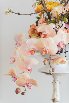 an arrangement of flowers in a vase hanging from a ceiling fixture on a white wall