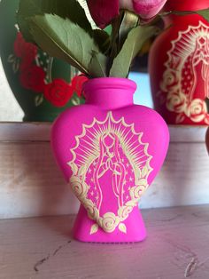 a pink vase with flowers in it sitting on a table next to two red vases