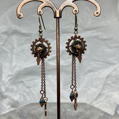 a pair of earrings with gears and chains hanging from it's hooks on a metal stand