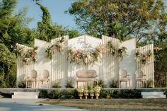 an outdoor wedding ceremony setup with chairs and flowers on the wall in front of it